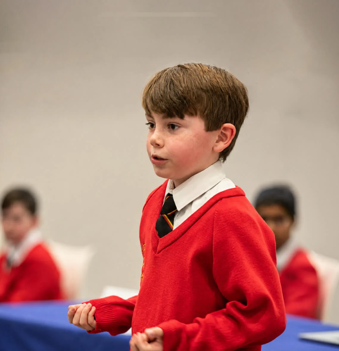 Young boy in a red school uniform speaking with hand gestures.